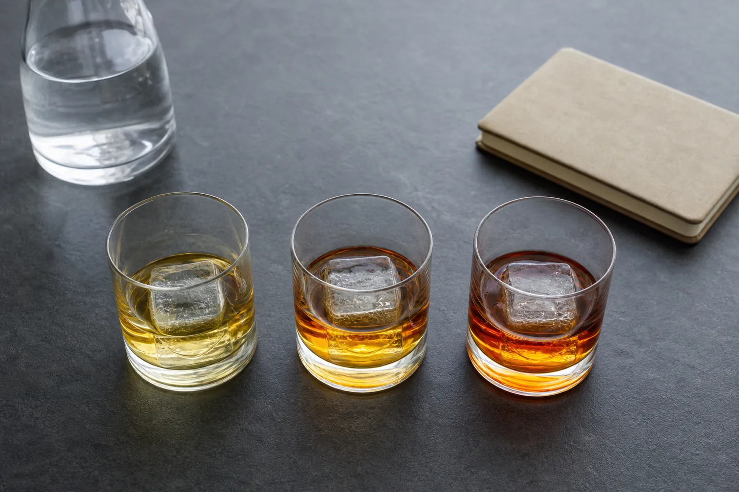 Tres vasos de whisky sin marca con cubos grandes de hielo y distintos tonos de ámbar